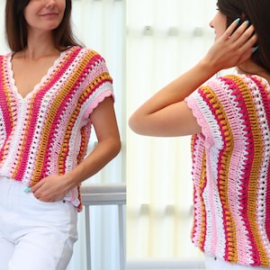 Puede incluir: Un top de ganchillo de manga corta y cuello en V, colorido. El top presenta rayas verticales en tonos rosa, blanco, amarillo y dorado. Los bordes de las mangas y el escote tienen un ribete festoneado. El top se combina con pantalones blancos.