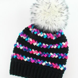 Puede incluir: Gorro de punto negro con un pomp&oacute;n de piel sint&eacute;tica blanca. El gorro tiene un patr&oacute;n de rayas de colores con hilo rosa, azul y blanco.