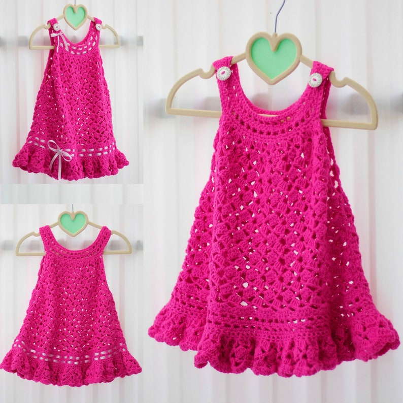 May include: A pink crocheted baby dress with a ruffled hem and white buttons. The dress is hanging on a heart-shaped hanger.