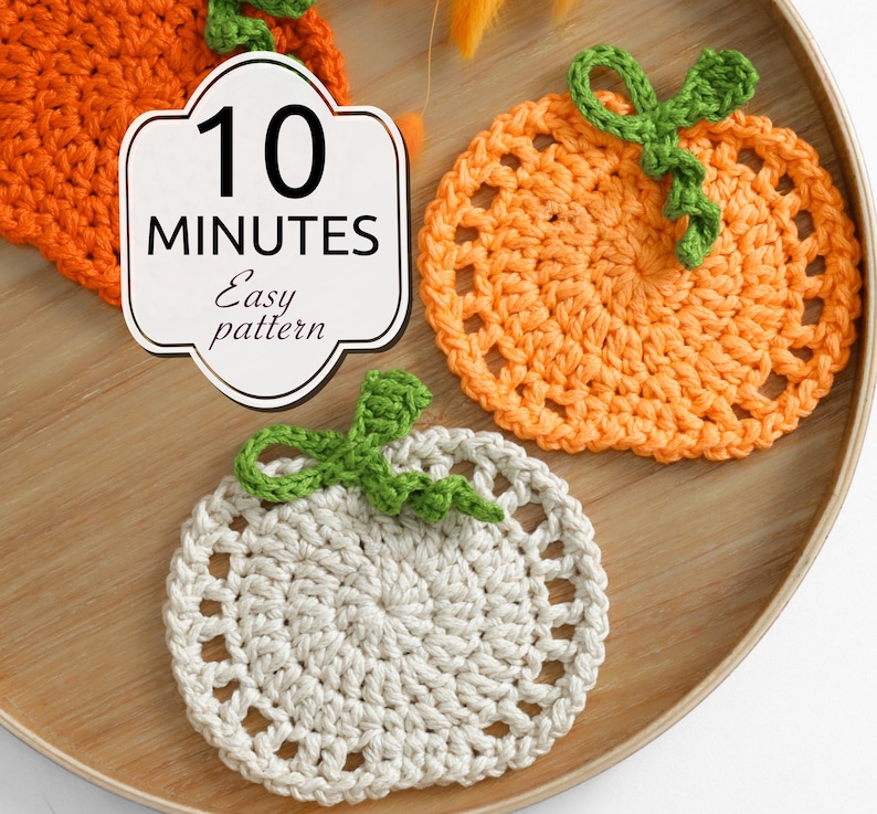 May include: Two round crochet coasters shaped like pumpkins, one orange and one off-white, each featuring a green stem and vine. A white label with a decorative border displays the text 10 MINUTES Easy pattern in black font.