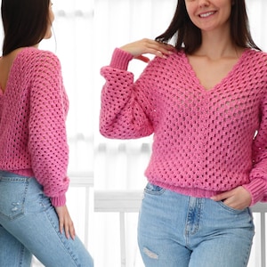 Pode incluir: Um su&eacute;ter de croch&ecirc; rosa com decote em V e design de costas abertas. O su&eacute;ter tem um caimento solto e mangas compridas.