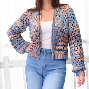 May include: A crocheted cardigan in shades of blue, tan, and brown. The open-front sweater has long sleeves and a textured, open weave design. The garment is paired with blue jeans.