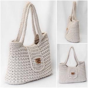 Puede incluir: Un bolso tote de crochet de color crema con un cierre dorado. El bolso tiene una parte superior ancha y abierta y dos asas largas.
