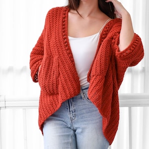 May include: A rust-colored crochet cardigan with a V-neck and long sleeves. The cardigan has a loose fit and a slightly cropped length.