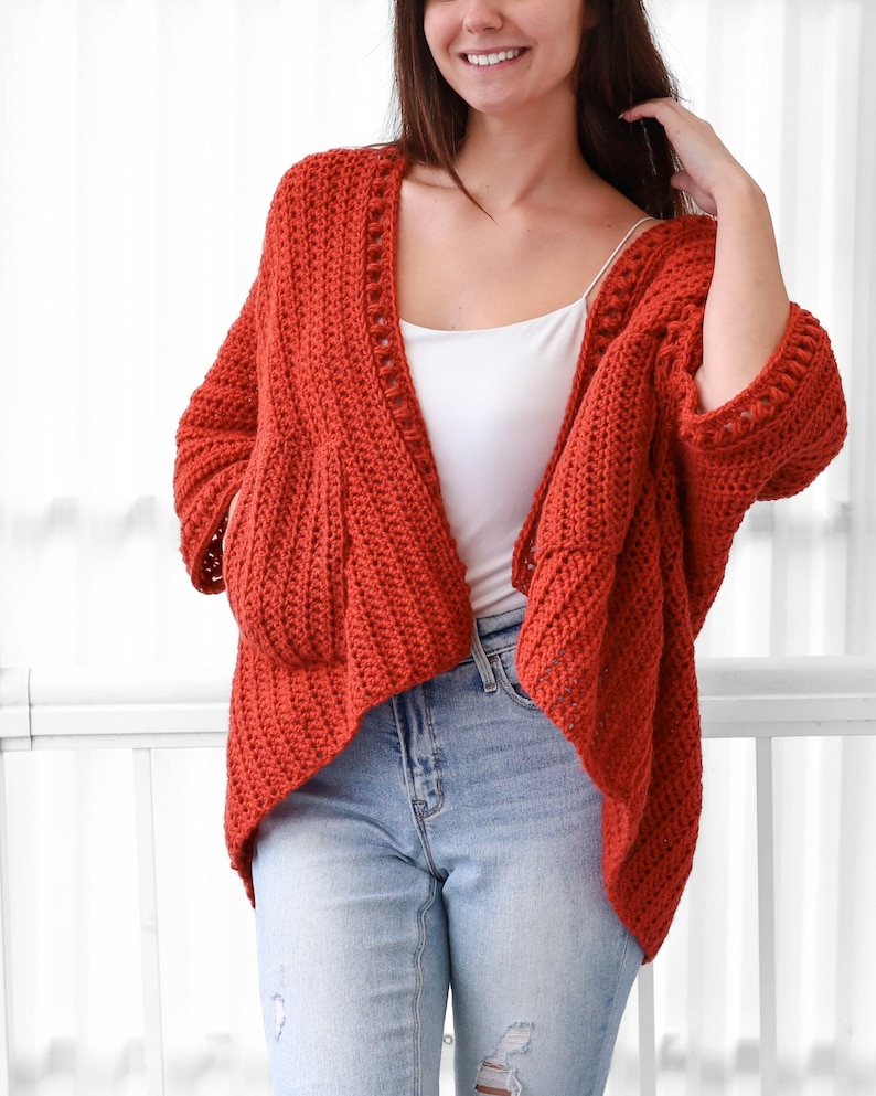 May include: A rust-colored crochet cardigan with a V-neck and long sleeves. The cardigan has a loose fit and a slightly cropped length.