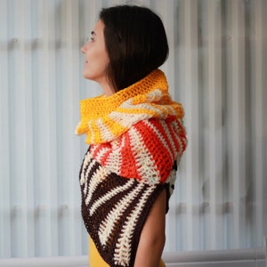 May include: A crocheted cowl in a multi-colored striped pattern. The cowl is made of brown, white, orange, and yellow yarn. The cowl is worn by a person with long brown hair.