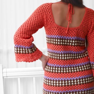May include: A crochet dress with a square neckline and bell sleeves. The dress is made with a multi-colored striped pattern in shades of orange, brown, purple, and white.