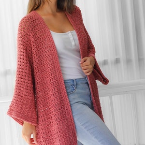 Pu&ograve; includere: Un cardigan in crochet rosa polvere con una vestibilit&agrave; ampia e maniche larghe. Il cardigan &egrave; aperto sul davanti e ha un design semplice ed elegante.