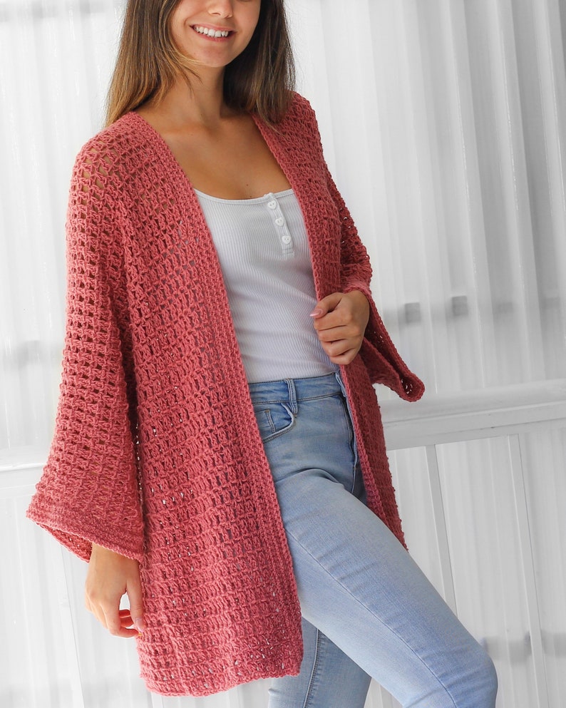 Pu&ograve; includere: Un cardigan in crochet rosa polvere con una vestibilit&agrave; ampia e maniche larghe. Il cardigan &egrave; aperto sul davanti e ha un design semplice ed elegante.