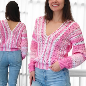 Może przedstawiać: Różowy i biały sweter z szydełka w paski z dekoltem w serek. Sweter z długim rękawem ma falisty dekolt oraz prążkowany dół i mankiety. Modelka ma na sobie jasnoniebieskie dżinsy.