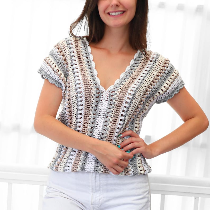 Puede incluir: Top de crochet de manga corta con cuello en V en una paleta de colores neutros de blanco, gris y beige. El top presenta un borde festoneado a lo largo del escote y las mangas. El dise&ntilde;o de crochet tiene un tejido abierto texturizado.