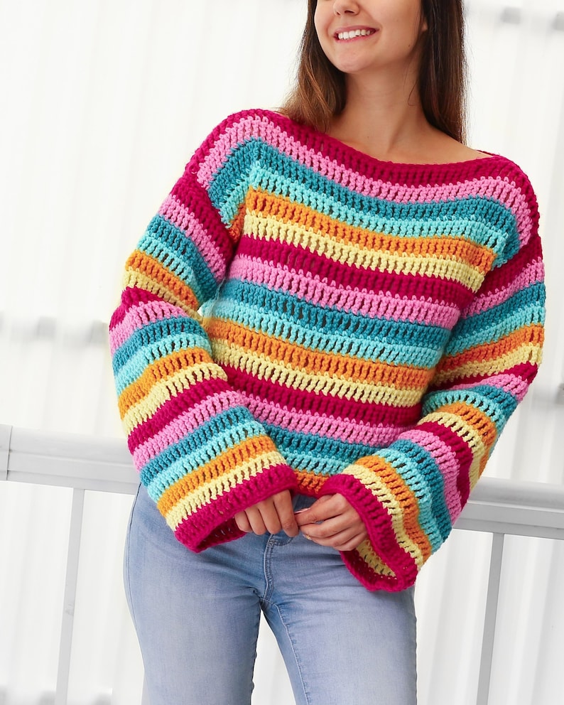 Peut inclure: Un pull en crochet ray&eacute; color&eacute; &agrave; manches longues et &agrave; la coupe ample. Le pull est r&eacute;alis&eacute; avec une vari&eacute;t&eacute; de couleurs vives, dont le rose, le bleu, le jaune et l'orange.