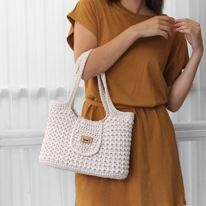 Puede incluir: Un bolso tote de crochet blanco con cierre de broche dorado. El bolso tiene un dise&ntilde;o simple y casual, perfecto para el uso diario.