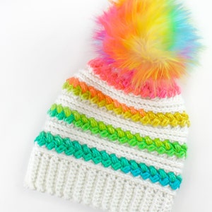 Puede incluir: Gorro de punto blanco con un patr&oacute;n de rayas arco&iacute;ris y un pomp&oacute;n arco&iacute;ris esponjoso.