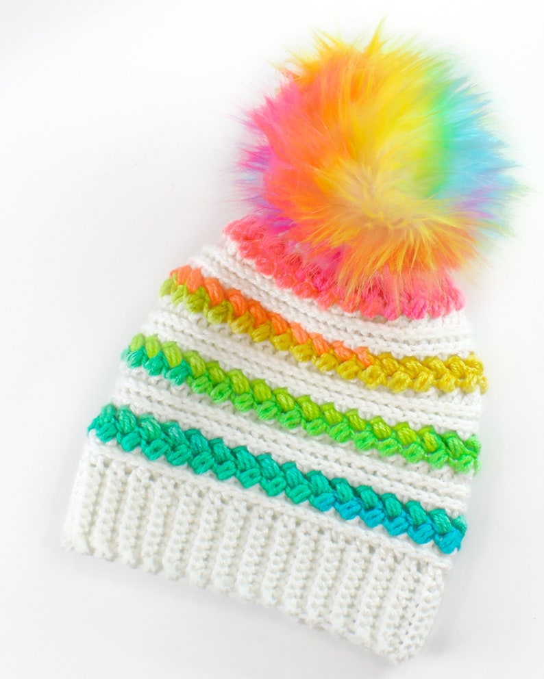 Puede incluir: Gorro de punto blanco con un patr&oacute;n de rayas arco&iacute;ris y un pomp&oacute;n arco&iacute;ris esponjoso.