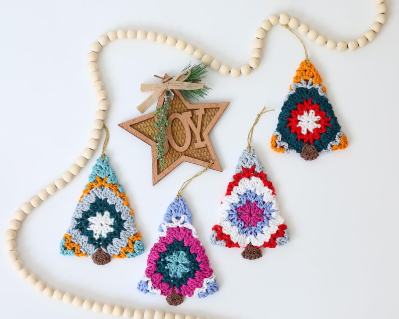 Puede incluir: Cuatro adornos de &aacute;rbol de Navidad de ganchillo en varios colores, incluidos rojo, azul, verde, amarillo y blanco. Los adornos cuelgan de una guirnalda de cuentas de madera con un recorte de estrella de madera que dice "ALEGR&Iacute;A".