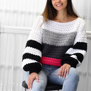 May include: A white, gray, black, and pink striped crocheted sweater with long sleeves and a wide neckline.