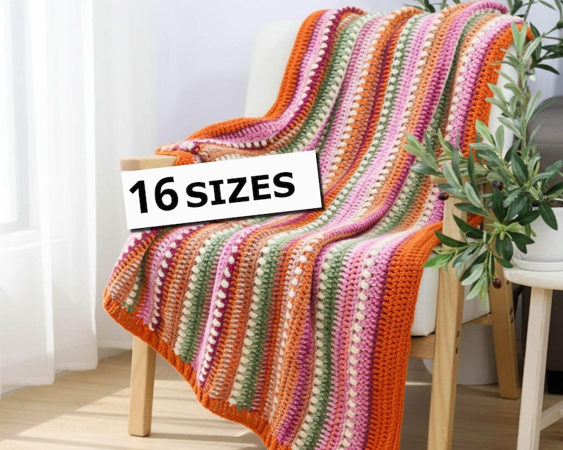 Pu&ograve; includere: Una coperta all'uncinetto a righe colorate, arancione, rosa, verde e bianco, drappeggiata su una sedia. Il testo "16 SIZES" &egrave; visibile. Questa coperta fatta a mano &egrave; un elemento decorativo per la casa.