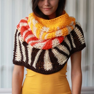 May include: A colorful crocheted cowl with stripes of orange, yellow, and white. The cowl is worn by a person with long brown hair. The cowl is made with a brown, white, and cream striped pattern.