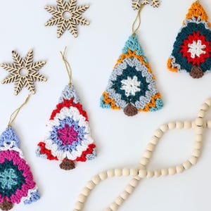 Puede incluir: Cinco adornos de &aacute;rbol de Navidad hechos a crochet en varios colores, incluyendo rojo, azul, verde, blanco y amarillo. Los adornos cuelgan de una cuerda blanca y est&aacute;n sobre un fondo blanco.