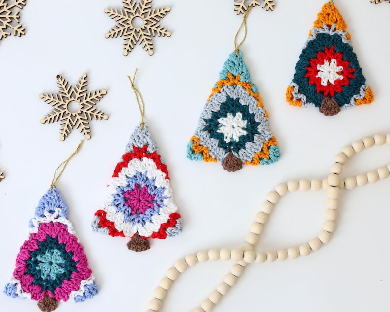 Puede incluir: Cinco adornos de &aacute;rbol de Navidad hechos a crochet en varios colores, incluyendo rojo, azul, verde, blanco y amarillo. Los adornos cuelgan de una cuerda blanca y est&aacute;n sobre un fondo blanco.