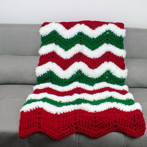May include: A red, white, and green crocheted blanket with a chevron pattern. The blanket is made with fluffy yarn and has a scalloped edge.