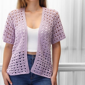 May include: A light purple crochet cardigan with a V-neck and short sleeves. The cardigan is made with a delicate open stitch pattern.