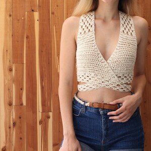 Puede incluir: Un top blanco de crochet con escote en V profundo y estilo de envoltura. El top se lleva sobre unos pantalones cortos de mezclilla azul.