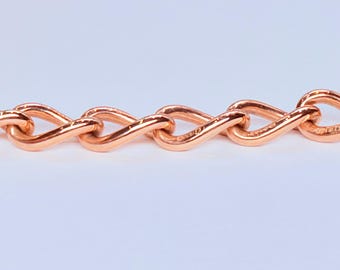 May include: A rose gold-toned chain bracelet featuring a series of interlocking, twisted oval links. The metal has a polished, reflective surface, creating a continuous, repeating pattern of connected loops arranged in a horizontal line.