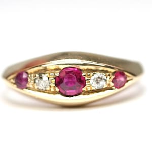 May include: A gold ring with a central oval ruby, flanked by two smaller rubies and two diamonds. The ring has a smooth, polished band and a decorative setting for the gemstones. The ring is set against a white background.