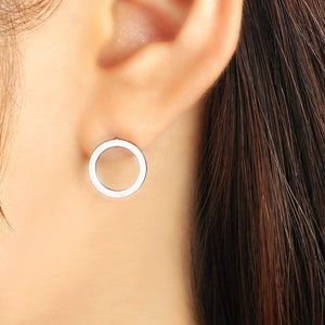 May include: A pair of silver hoop earrings with a simple, circular design. The earrings are worn in the earlobe of a person with long brown hair.