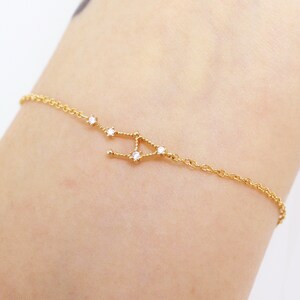 This photo shows the front of a gold Libra horoscope bracelet hanging on a woman's wrist.