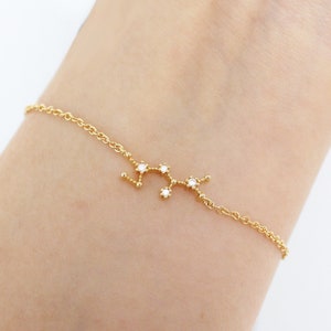 This photo shows the front of a gold Sagittarius zodiac bracelet hanging on a woman's wrist.