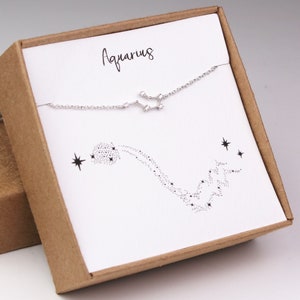 This photo shows the front of a silver Aquarius zodiac bracelet hanging on the matching Aquarius card in a gift box.