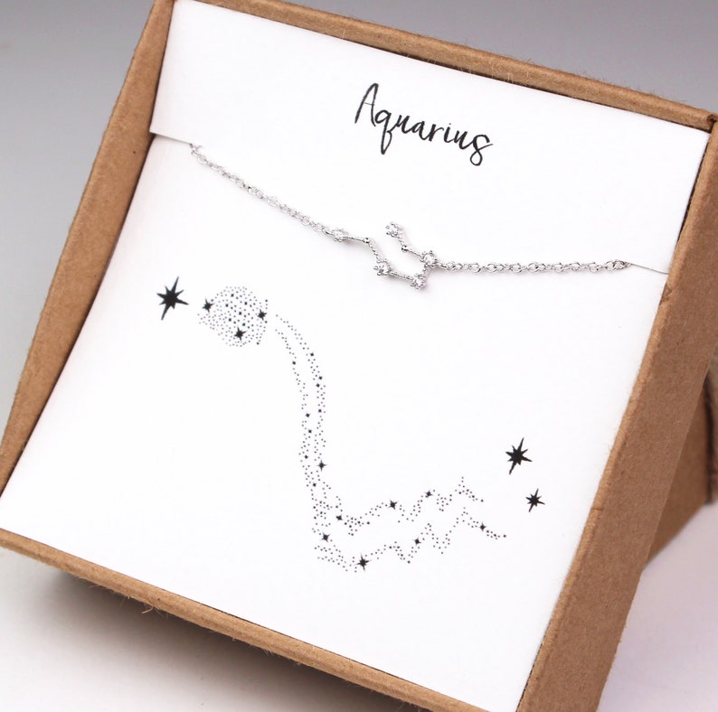 This photo shows the front of a silver Aquarius constellation bracelet hanging on the matching Aquarius card in a gift box.