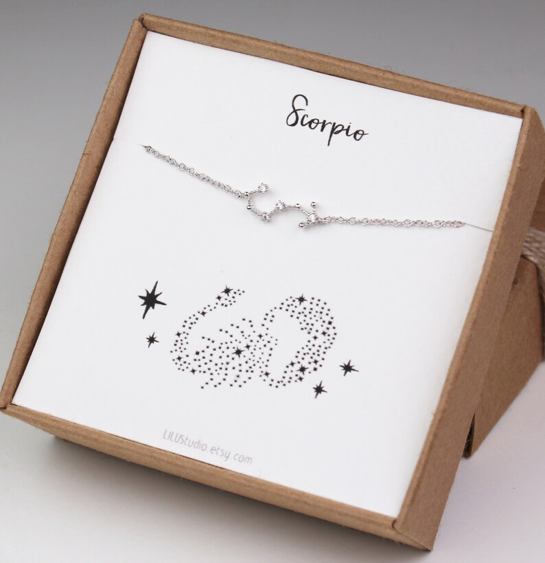 A silver Scorpio zodiac bracelet is hanging on the matching Scorpio card in a gift box.