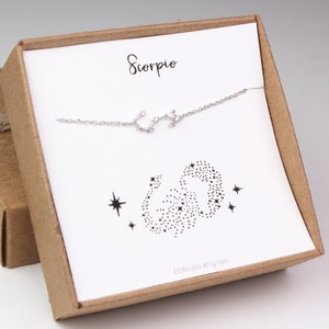 A silver Scorpio horoscope bracelet is hanging on the matching Scorpio card in a gift box.