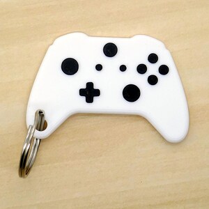 May include: White plastic keychain shaped like a video game controller with black buttons.