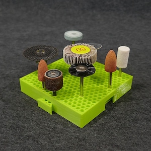 May include: A green plastic storage organizer with a honeycomb design holds a variety of sanding and polishing tools. The tools include a sanding disc labeled "80", a small brush, a cone-shaped sanding tool, and a white felt polishing tool.