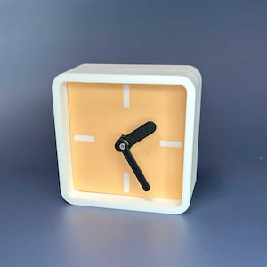 May include: A square, white alarm clock with a light orange face. The clock has black hands and white markers at each hour. The clock is a cube shape and sits on a blue surface.