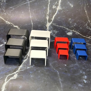 May include: A collection of small, open-top, rectangular display stands in various colors. Sets of three stands are in black, white, red, and blue. The stands are arranged in a stepped configuration, with each stand slightly smaller than the one below.