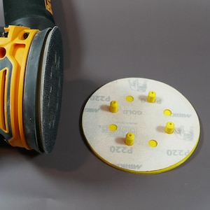 May include: A white sanding disc with yellow hook and loop fasteners and the text "Mirka P220" printed on the edge. There are six yellow plastic posts on the disc.