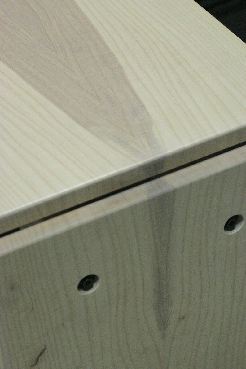 May include: Close-up of a light wood cabinet with a visible grain pattern. The cabinet has two small black screws on the front.