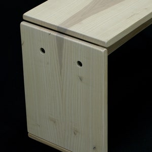 May include: A light wood bench with a unique design. The bench has a rectangular top and a curved, L-shaped base. The wood grain is visible on the surface of the bench.