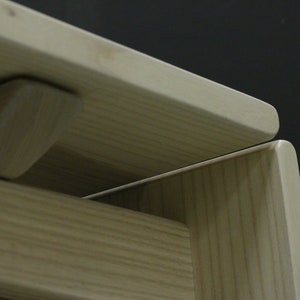 May include: Close-up of a wooden table with a natural finish. The table top is made of two pieces of wood that are joined together with a subtle seam. The table has a simple, modern design.