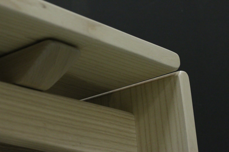 May include: Close-up of a wooden table with a natural finish. The table top is made of two pieces of wood that are joined together with a subtle seam. The table has a simple, modern design.