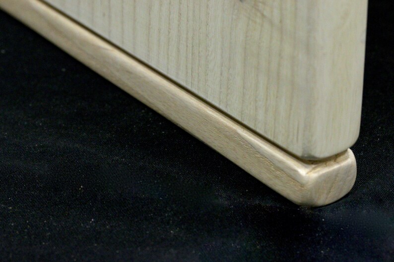 May include: Close-up of the bottom of a wooden table leg with a rounded edge. The leg is made of light wood with a natural finish.