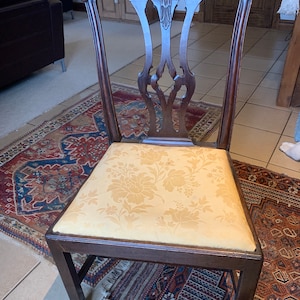 May include: A dark wood chair with a carved back and a floral patterned seat cushion. The chair is sitting on a patterned rug.