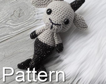 May include: A gray and black crocheted mermaid goat amigurumi toy with sparkly black tail and black eyes. The toy is sitting on a white fluffy surface. "Pattern" is written in white letters on the bottom of the image.