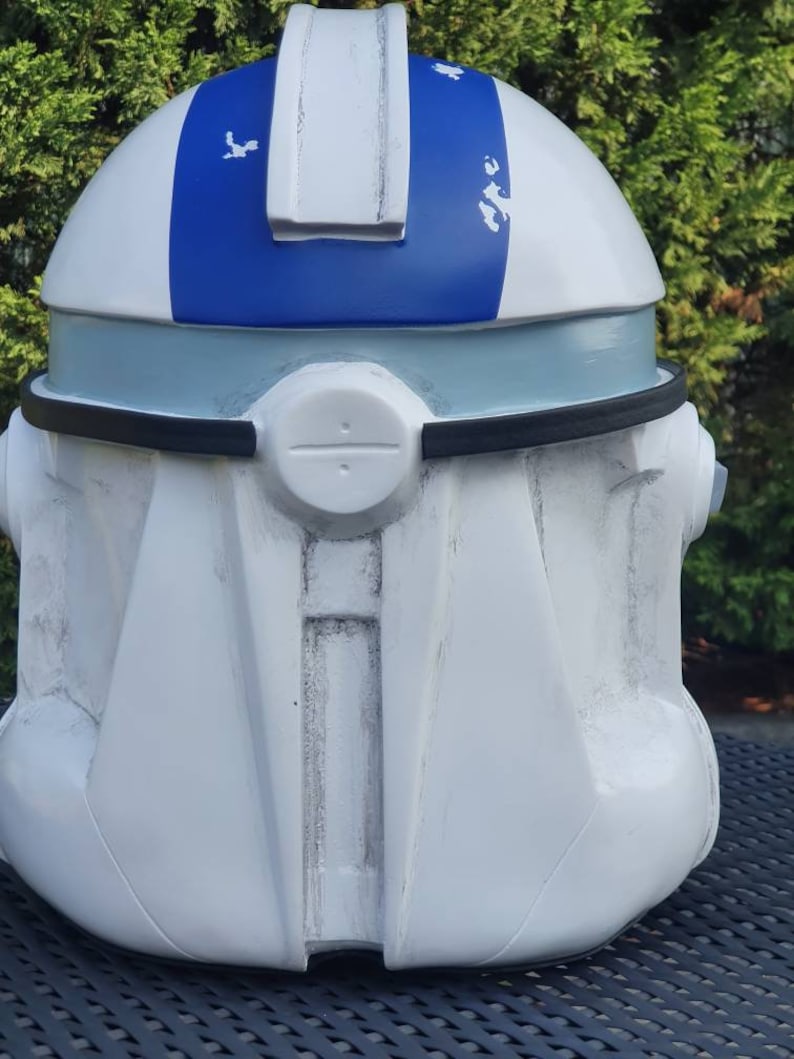 May include: A white and blue helmet with a distinctive design. The helmet features a blue stripe across the top and a light blue band around the middle. The helmet has a black trim and a circular detail on the front. The overall aesthetic suggests a futuristic or sci-fi theme.